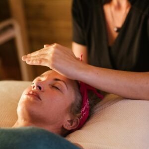 Relaxed woman with closed eyes lying under blanket while getting reiki therapy treatment from unrecognizable therapist in cozy salon with blurred background